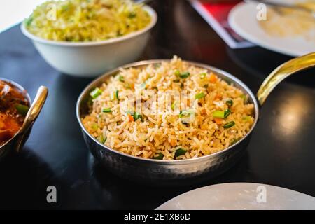 Selective focus of Vegetable Fried Rice served in a wok pan on a black table.