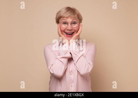 Mature woman in glasses being surprised with news. Studio shot Stock Photo