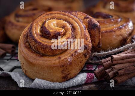 Fresh baked cinnamon buns on a wire rack with cinnamon sticks Stock Photo