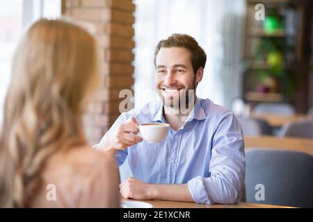 Smiling millennial guy drinking coffee with his girlfriend at cafe, having fun conversation during breakfast Stock Photo