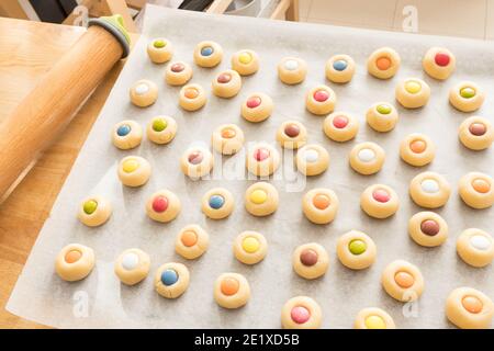 Closeup view of a lot of cookies with different colored chocolate pieces on top of them on a baking paper. Stock Photo