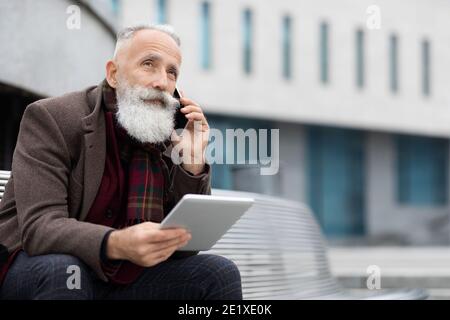 Elderly man holding digital tablet and talking on phone Stock Photo
