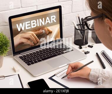 Young woman office worker taking notes while listening to webinar Stock Photo