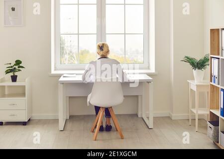 Doctor sitting at desk in hospital office, working on computer or doing paperwork Stock Photo