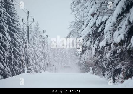 Transportation during winter weather. Car driving on snow covered road in the middle of forest during snowing. Stock Photo