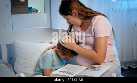 Young pregnant mother hugging and soothing her crying little boy lying in bed at night. Caring and loving parent hugging child Stock Photo