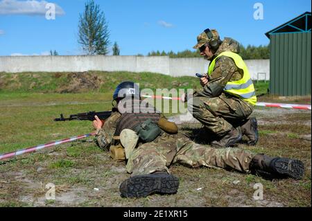 On a military shooting range: fully equipped soldier aiming at cockshies with a Kalashnikov machine gun, instructing officer watching Stock Photo
