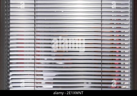 Slightly closed white blinds on the study window. Background with horizontal blinds. Stock Photo