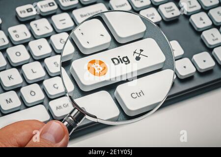 magnifying glass in hand focused on computer key with bitcoin symbol and dig word with symbol Stock Photo
