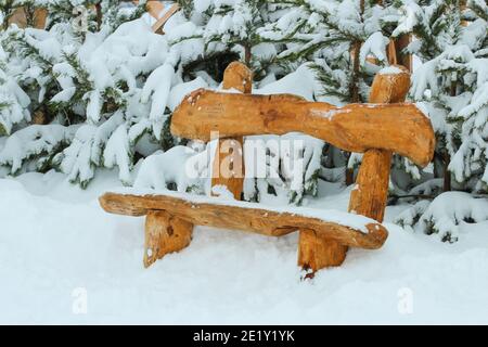 Wooden bench made of logs among snow-covered pine trees in the park Stock Photo