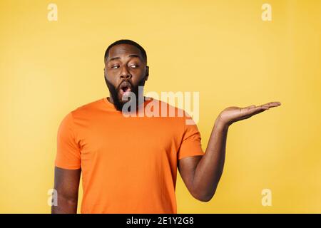 Surprised black man holds something in hand. Yellow background Stock Photo