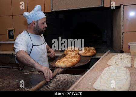 Daily production of bread baked with wood oven with traditional method.A baker making Turkish pita bread.Baker taking fresh Turkish pita bread from ov Stock Photo