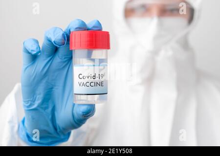 Covid 19 vaccine bottle in doctors hand. Doctor in protective suit, face mask, safety googles and rubber gloves demonstrate vaccine against Stock Photo