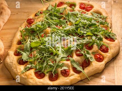 Apulian focaccia, typical  pizza from Bari with cherry tomatoes and rocket leaves on wooden table Stock Photo