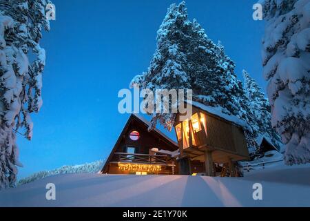 Fantastic winter landscape with wooden house with light in windows in snowy mountains and night sky. Christmas holiday and winter vacations concept Stock Photo