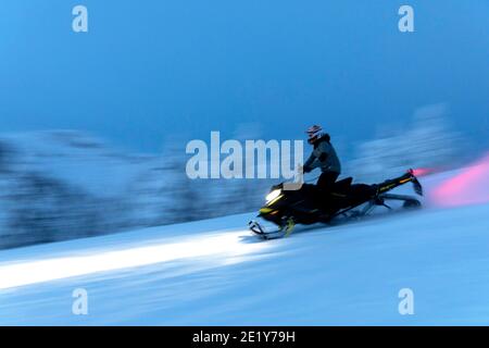 Snowmobilers enjoy a fresh-air outing on woodsy trails at twilight, Stock Photo