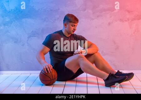 Athletic trainer with orange basketball ball on a bright neon background. Coach looking at her wrist watch. Interactive coach concept Stock Photo