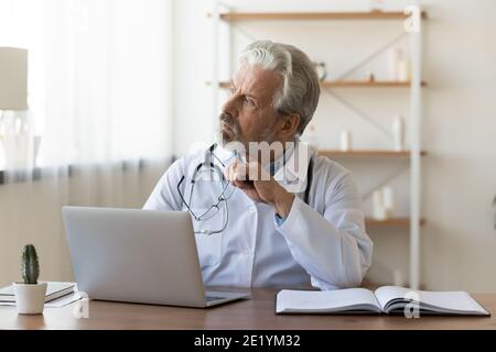 Thoughtful senior older male general practitioner looking in distance. Stock Photo