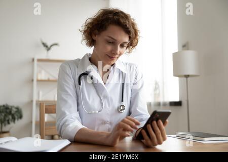 Smiling pleasant young female general practitioner using mobile phone. Stock Photo