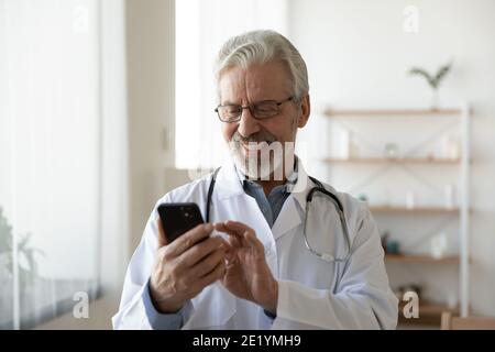 Happy old male doctor using mobile phone in clinic. Stock Photo