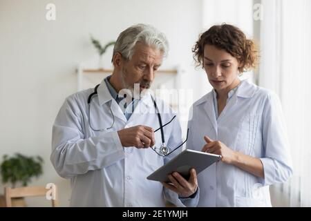 Serious old male doctor discussing test results with young colleague. Stock Photo