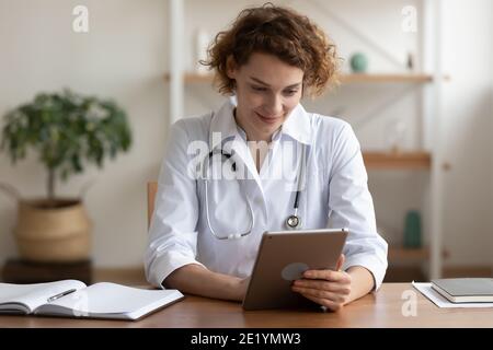 Happy young female general practitioner using digital computer tablet. Stock Photo