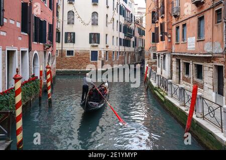 Traditional Venetian gondola with tourists on rio dei Bareteri canal in Venice, Italy Stock Photo