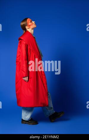 Female model in baggy coat walking against blue background Stock Photo