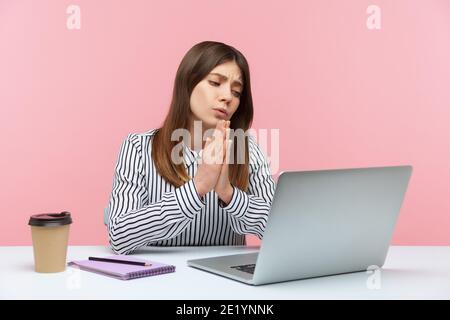 Business woman in striped shirt holding hands in praying gesture and talking on video call on laptop, asking heartily, pleading with desperate face. I Stock Photo