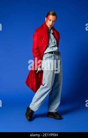Female model in baggy coat walking against blue background Stock Photo
