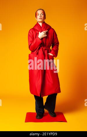Female model in trendy red coat against yellow background Stock Photo
