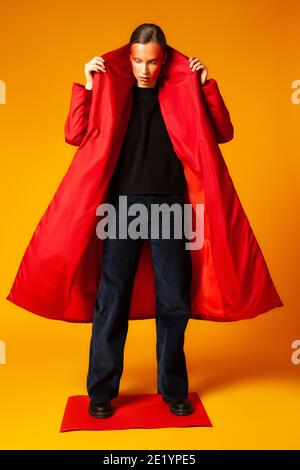 Female model adjusting trendy red coat against yellow background Stock Photo