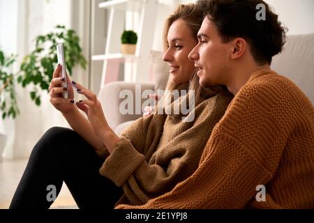 Young happy couple customers holding smartphone using mobile cell phone at home. Stock Photo