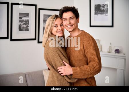 Happy young couple hugging looking at camera standing at home, portrait. Stock Photo