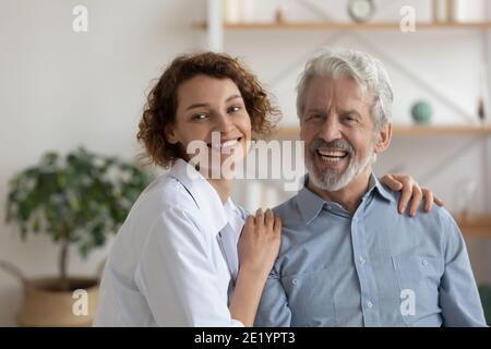 Dreamy pleasant nurse caregiver supporting elderly mature patient. Stock Photo