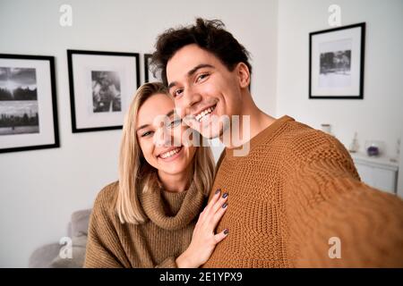 Happy young couple hugging looking at camera taking selfie at home, portrait. Stock Photo