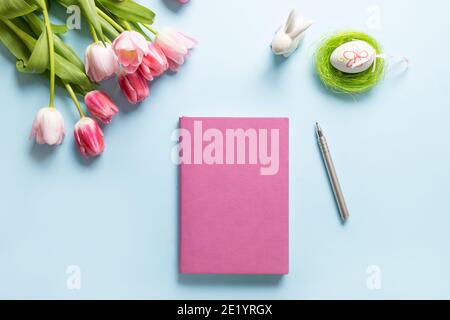 Easter planning with notebook, tulip flowers, egg on blue background. Top view with copy space. Happy Easter greeting card. Stock Photo