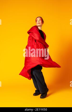 Female model in baggy coat spinning around against yellow background Stock Photo