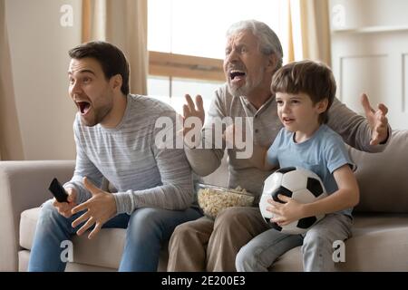 Three generations of men watch football at home Stock Photo