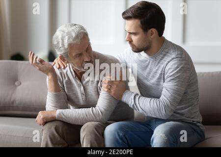 Caring adult son support upset senior dad at home Stock Photo