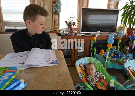 Young boy is looking after his baby brother while doing home work ,United Kingdom Stock Photo