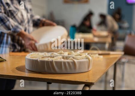 Selective focus. Close up of a tambourine on a work table during a native drum workshop. Persons handling drums in the blurrde background.  Stock Photo