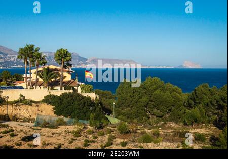 Mediterranean style house with spanish flag and palm trees with view on ocean and the rock 'Ifach' of Calpe, Albir, Costa Blanca, Spain Stock Photo