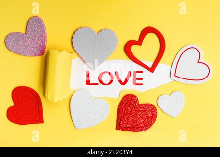 English text Love on a torn piece of yellow paper with romantic hearts. Stock Photo