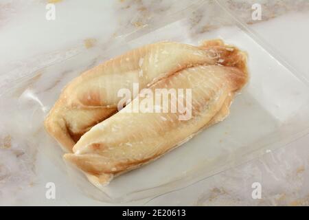 Two frozen raw tilapia fish fillets in vacuum packed airtight plastic container Stock Photo