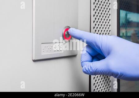 A man's hand in a protective medical glove presses the sos button in a modern electric train, close-up. Stock Photo