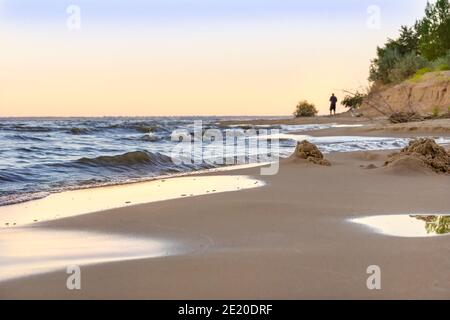 half-blurred ruins of a sand castle on a deserted beach, in the distance on the shore the silhouette of the man who built it, a symbol of a shaky, eas Stock Photo