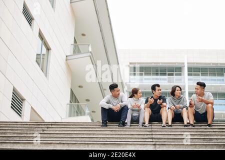 Group of friends sitting on steps and discussing healthy lifestyle after jogging together in the morning Stock Photo