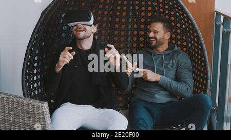 Virtual world. Happy homosexual couple wearing VR glasses and relaxing on the balcony. High quality photo Stock Photo