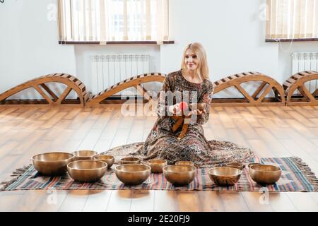 Woman playing on a tibetian singing bowl for sound therapy standing in yoga studio Stock Photo